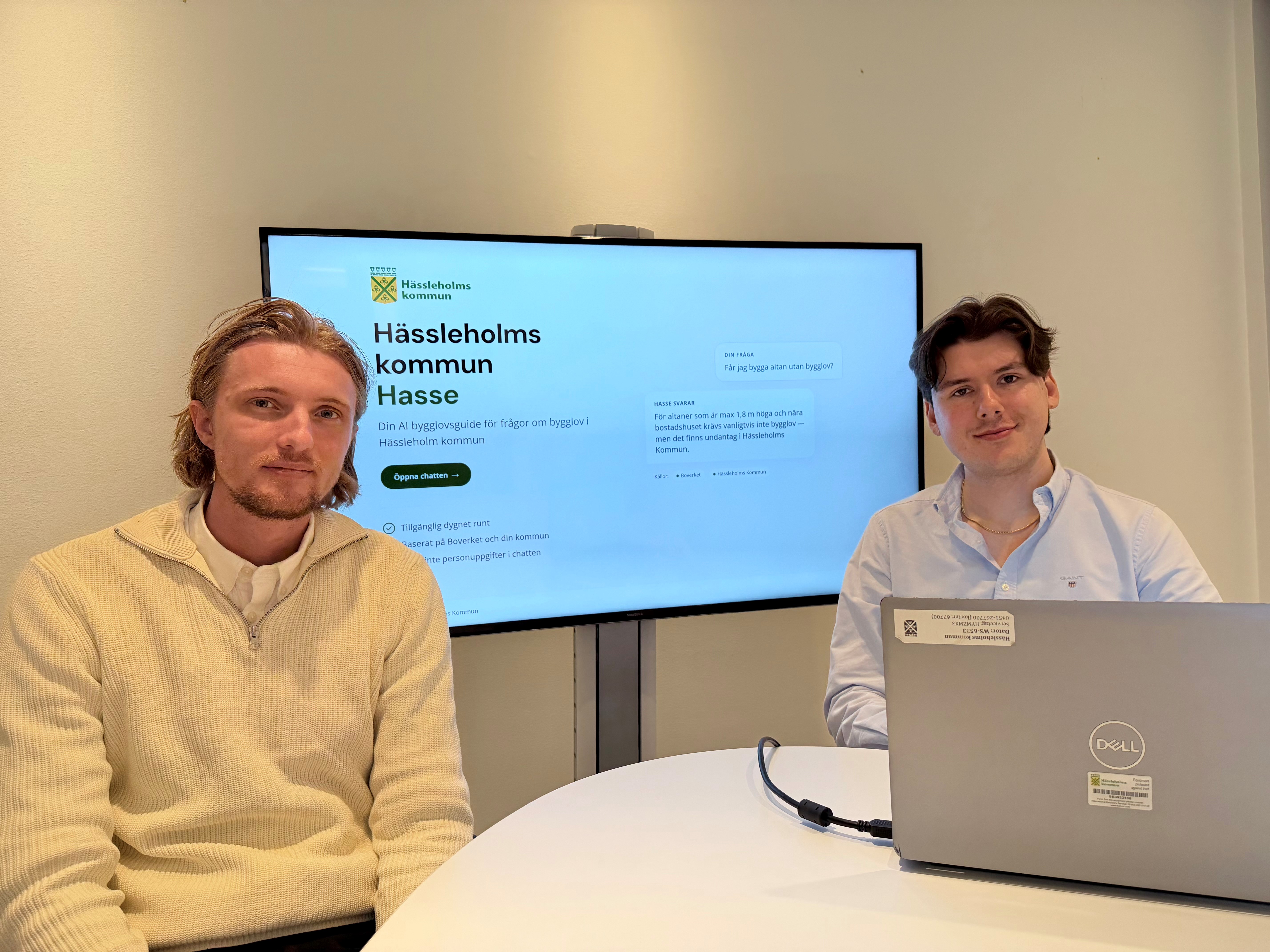 Byggnadsinspektör Noah och GIS-utvecklare David framför en TV-skärm som visar AI-assistenten Hasse.
